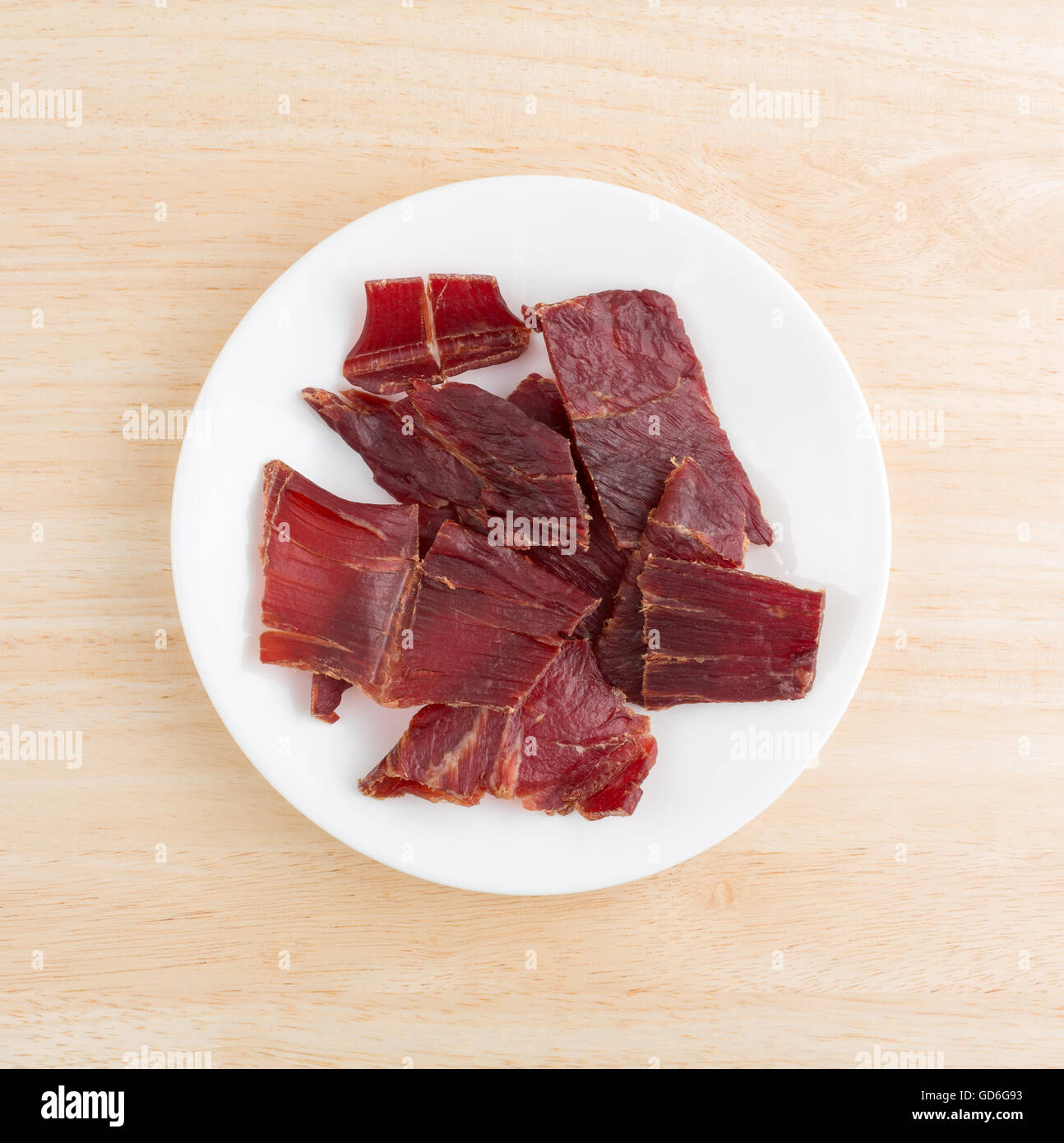 Draufsicht auf mehrere Scheiben von Laubholz geräuchert Dörrfleisch auf einem weißen Teller oben auf einer hölzernen Tischplatte. Stockfoto