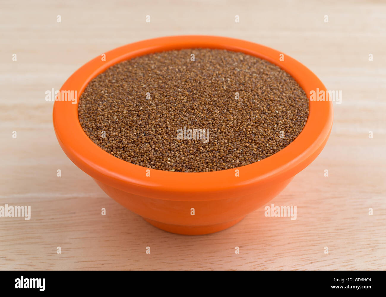 Teff Getreide füllen eine orange Schale auf einer hölzernen Tischplatte. Stockfoto