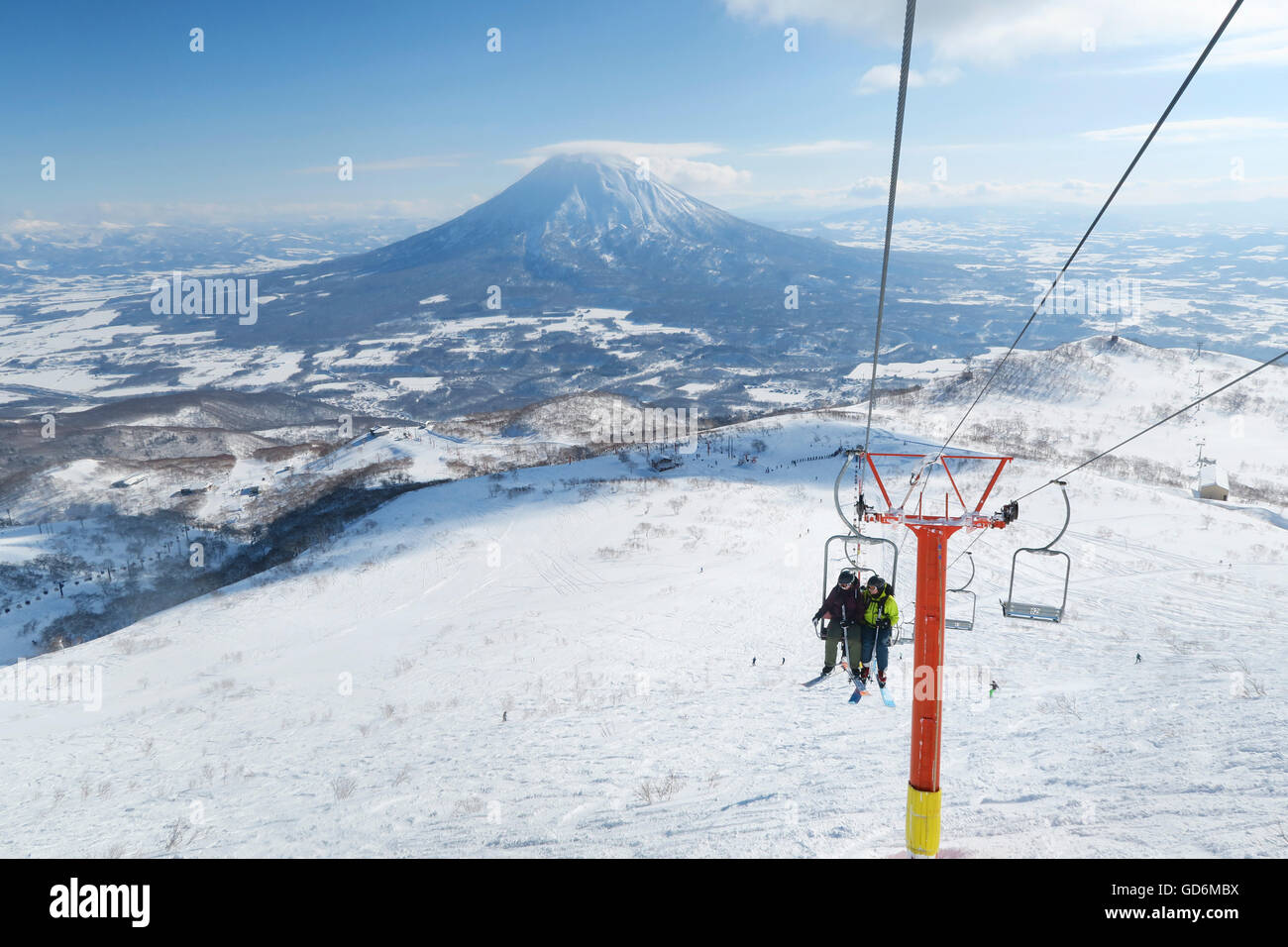 Mit dem Vulkan Yotei im Hintergrund ein weiblicher und männlicher Backcountry Skifahrer sitzen in einer Open-Air-Sessellift zum Gipfel des Mount Annupuri, im Skigebiet Niseko United auf der japanischen Insel Hokkaido.     Niseko United besteht aus vier Stockfoto