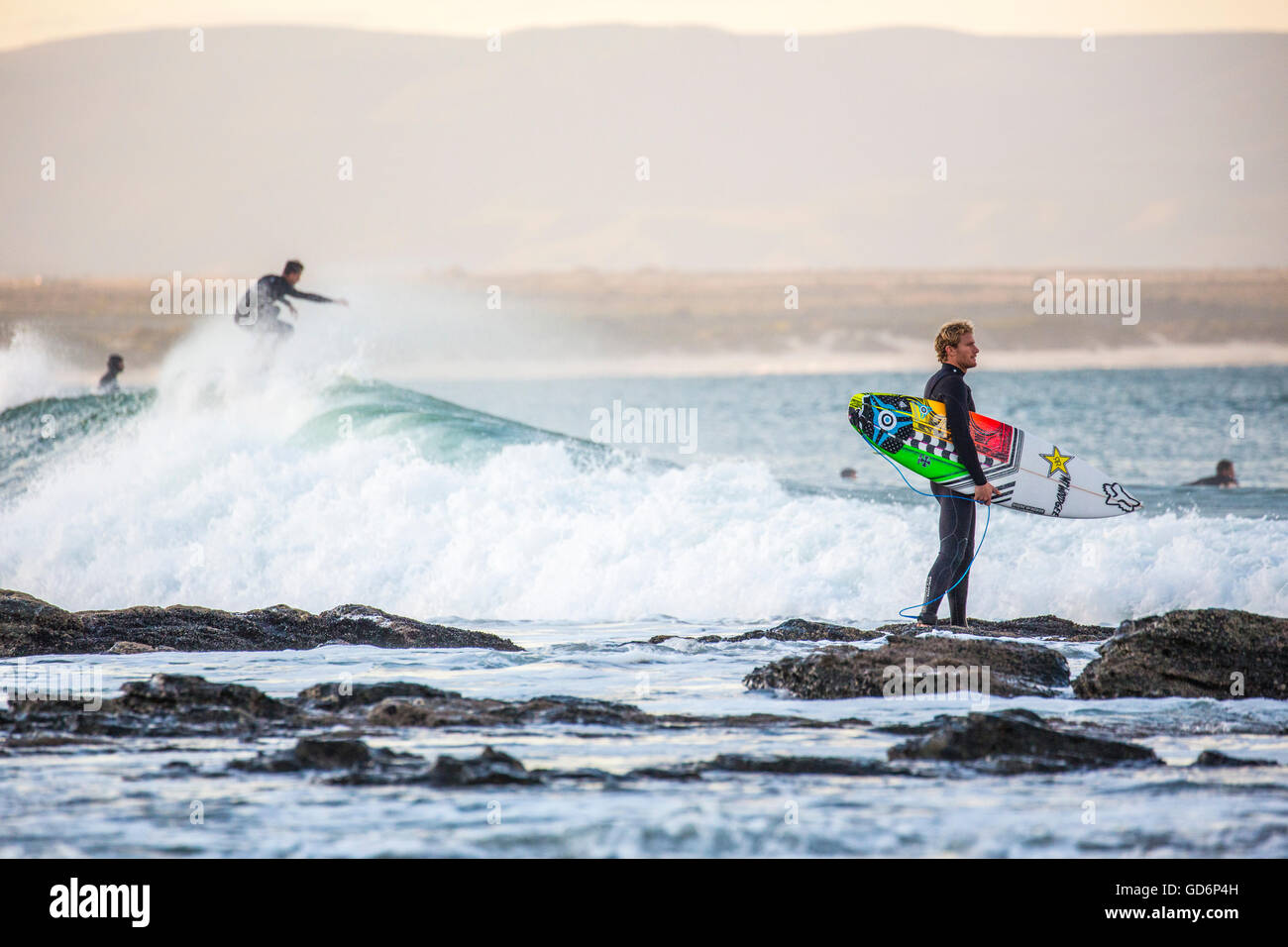 Surfer Uhren die Wellen, während andere Surfer Spaß im Hintergrund, Jefferys Bay, Südafrika haben Stockfoto