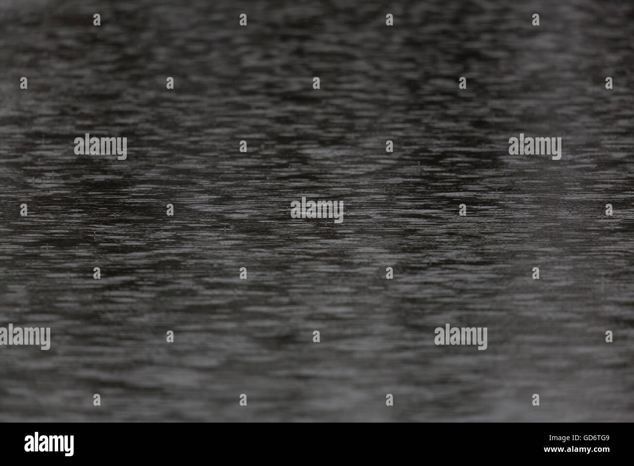 Natürliche Regentropfen und Kreise auf dunklen Wasseroberfläche Stockfoto