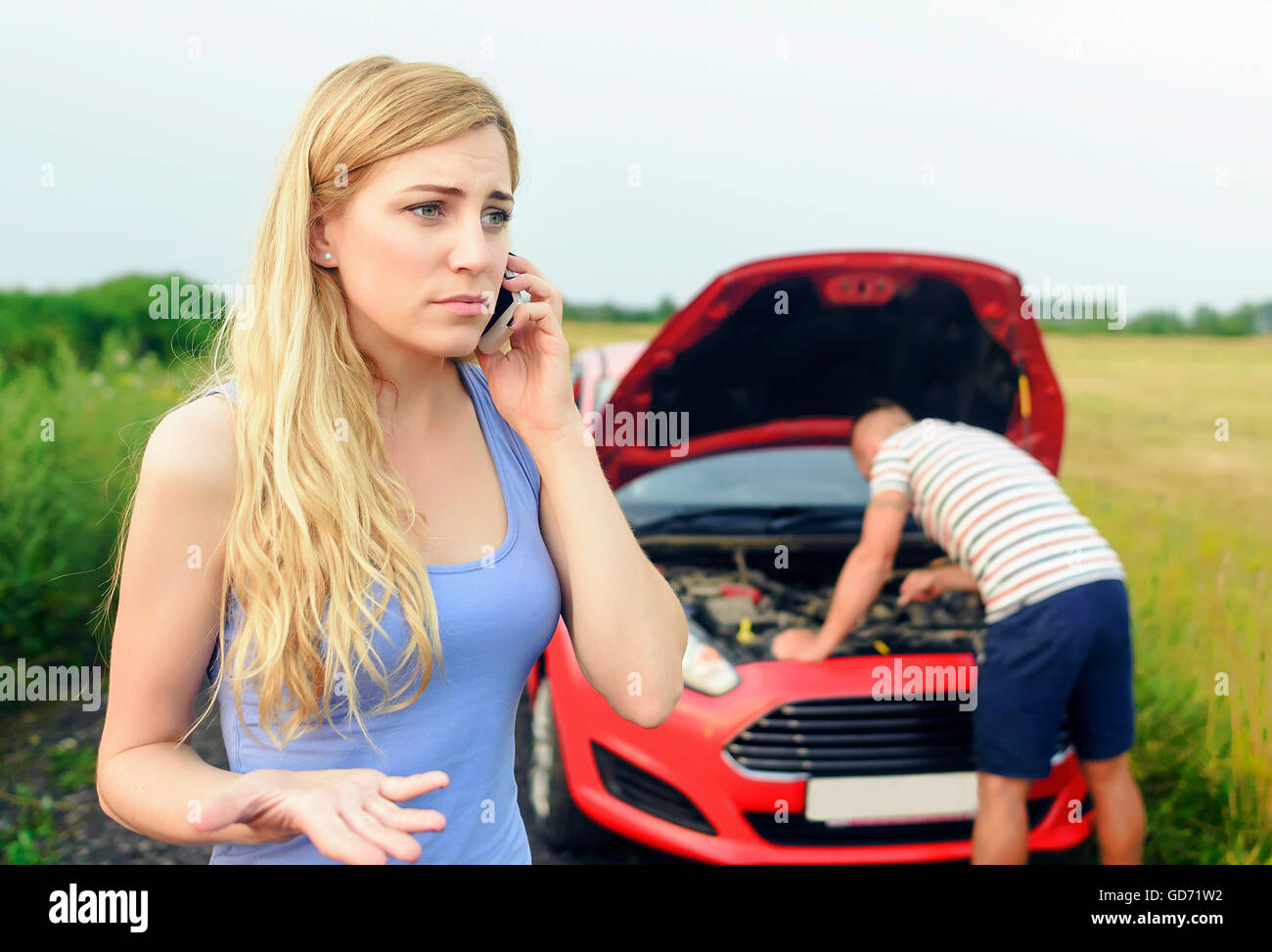 Junge blonde Frau Hilferuf auf dem Handy. Junges Paar kann nicht den Weg wegen dem kaputten Auto weiter. Schäden an auto. Stockfoto