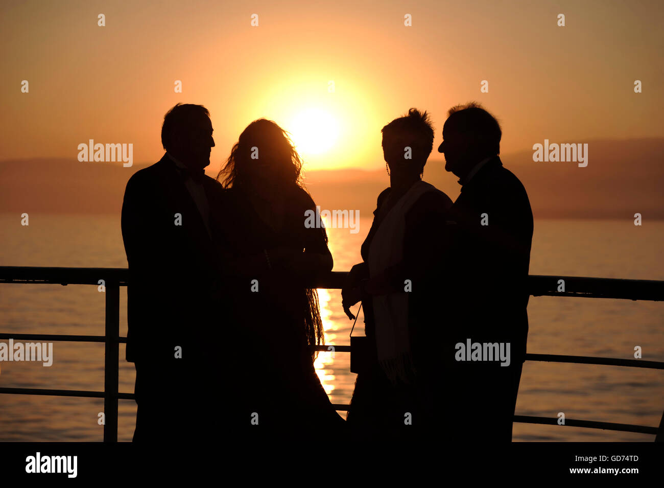 Gruppe von vier Personen auf dem Deck eines Kreuzfahrtschiffes bei Sonnenuntergang Stockfoto