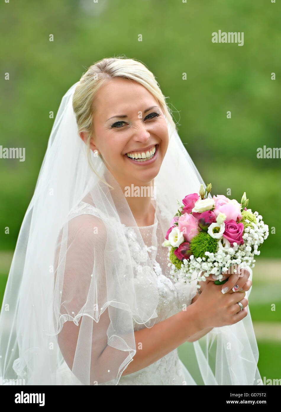 Lachende Braut im weißen Hochzeitskleid mit Brautstrauß und Schleier, Deutschland Stockfoto