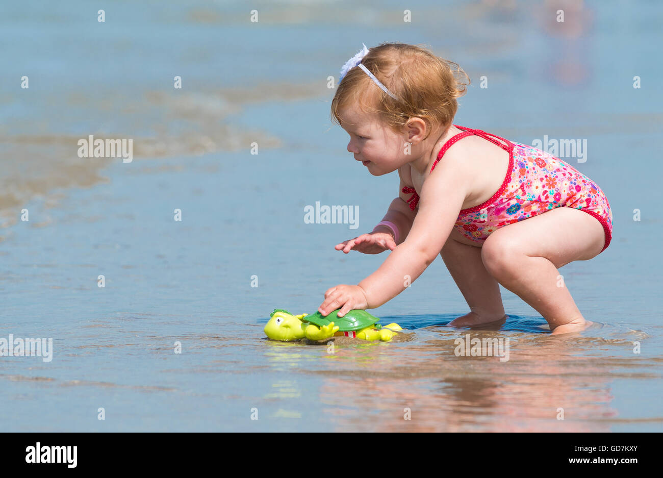 kleines Mädchen am Strand im Meer trägt sie eine bezaubernde Blume Badeanzug suchen in der Ferne entdecken und explo Stockfoto