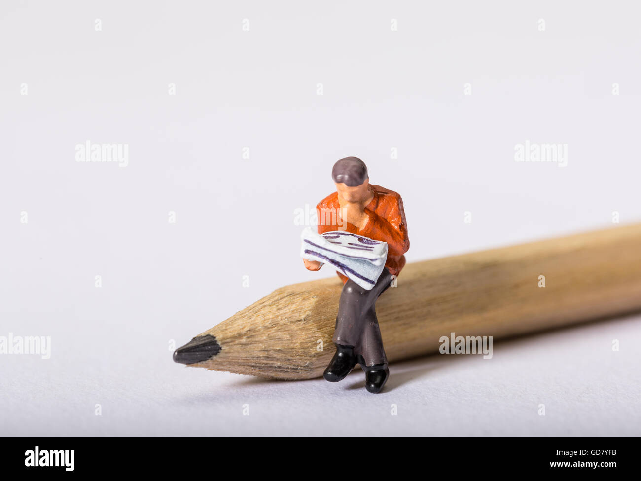 Konzept-Bild einer männlichen Figur durch eine Zeitung setzte sich auf einen Bleistift mit Blick auf ein Kreuzworträtsel oder auf der Suche nach einem Job suchen Stockfoto