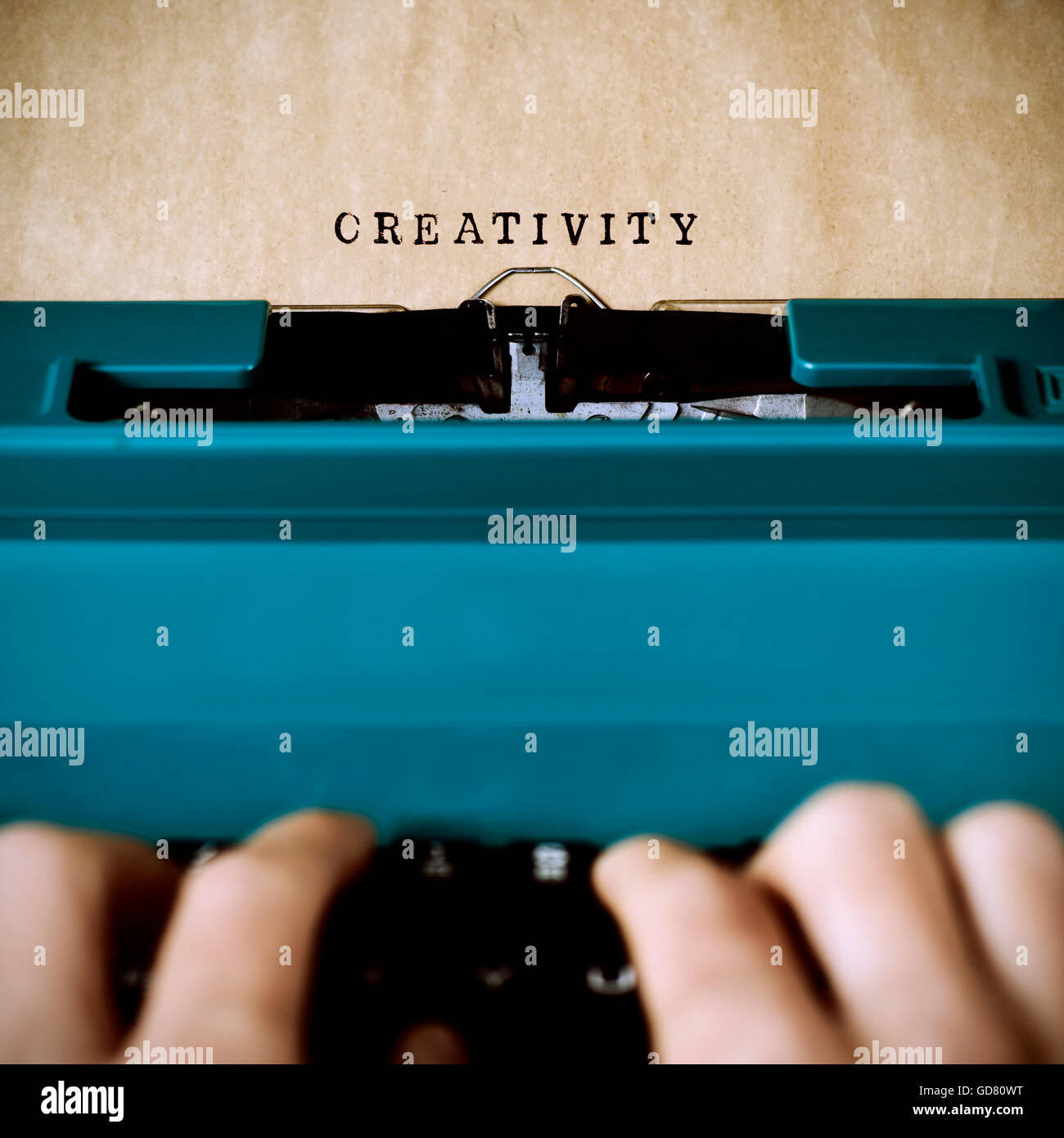 Nahaufnahme von den Händen eines jungen Mannes, der die Wort Kreativität in eine gelbliche Folie mit einer alten blauen Schreibmaschine Maschineschreiben Stockfoto