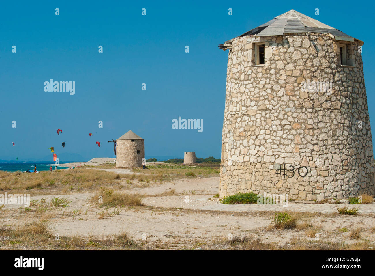 Alte Windmühlen an einem Strand, bevölkert von Windsurfer und Kitesurfer in Lefkada, Lefkas Stockfoto