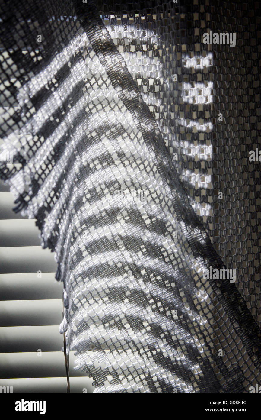 Sonnenlicht durch Jalousien werfen eine Muster von Licht und Schatten auf einem Bad Vorhang Stockfoto