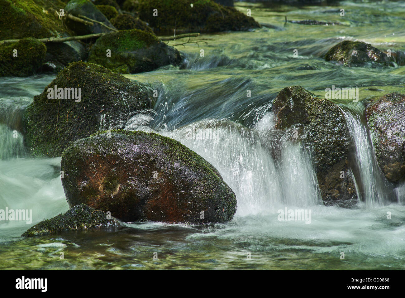 Bergwasser Fluss fließt durch Grün bemoosten Steinen Felsbrocken Stockfoto