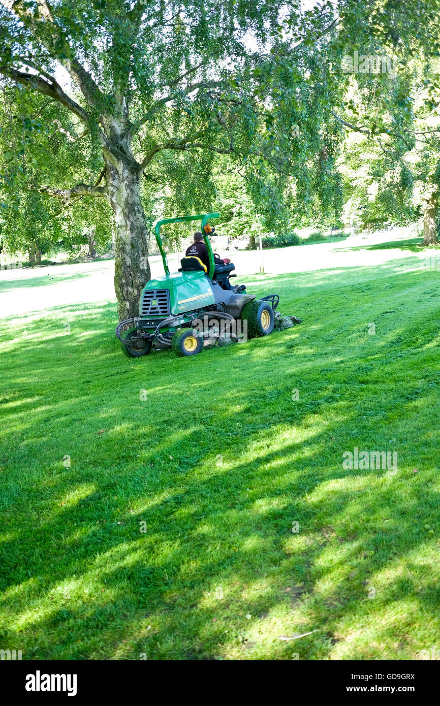 Ein Rat Arbeiter auf eine Fahrt auf Mäher mäht den Rasen in einem öffentlichen Park in einer englischen Kleinstadt Stockfoto