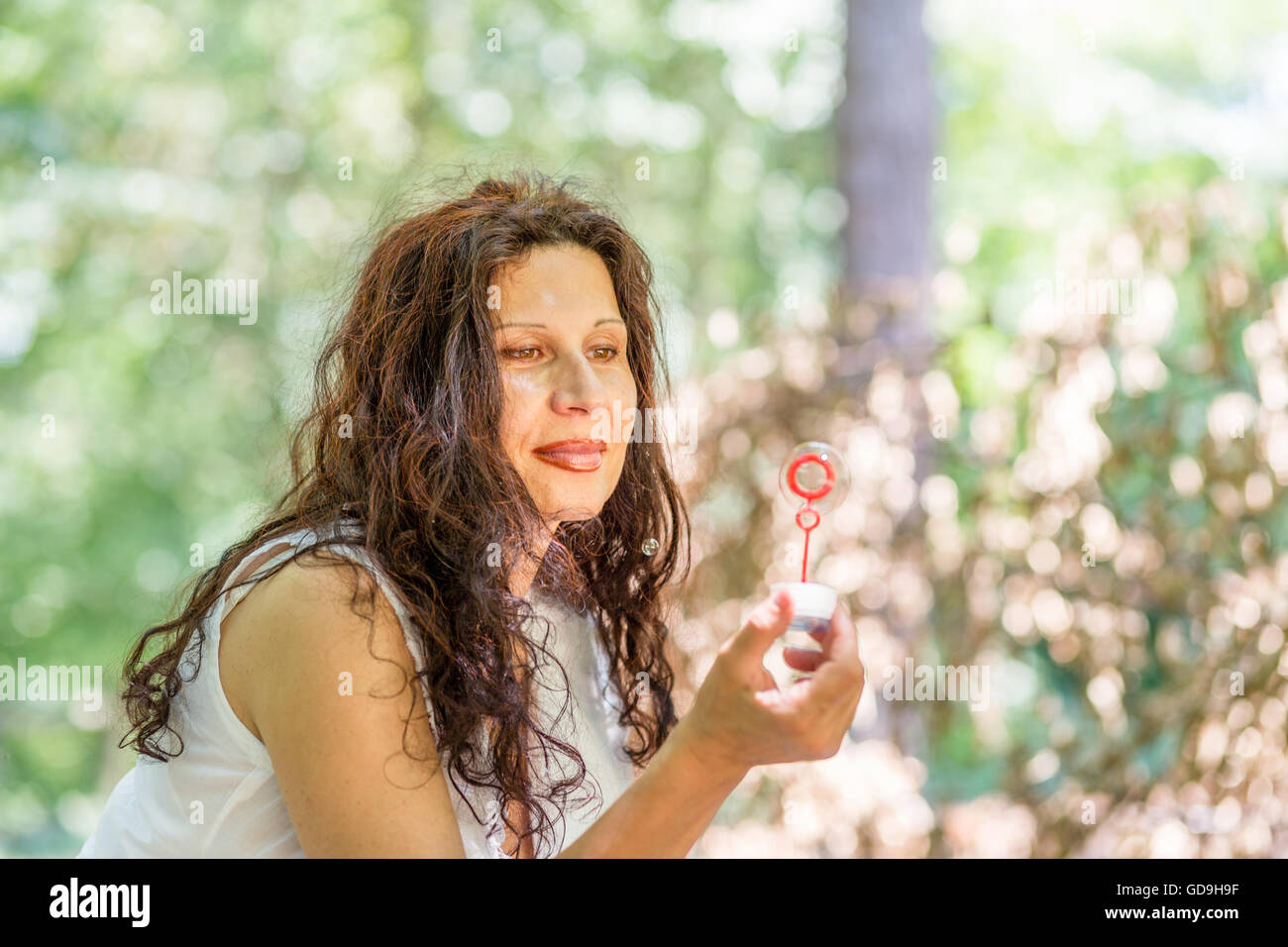schöne reife Erwachsene Frau spielt im Park Seifenblasen und hält eine mit Zauberstab betrachten Stockfoto