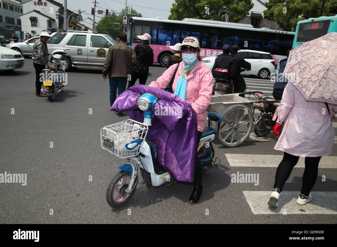 Frau mit einer Jacke, die Hände unter einer Decke und Gesicht bedeckt gegen  Verschmutzung reitet einen Roller auf einem Zebrastreifen, andere sind auch  auf Stockfotografie - Alamy