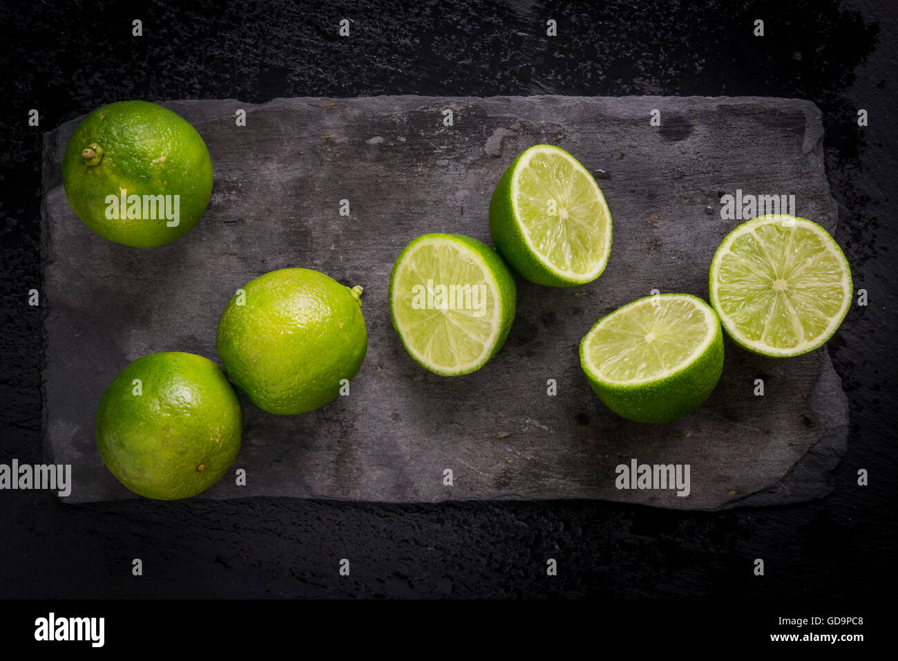 Ganze und geschnittene Limetten auf Schiefer Tafel. Ansicht von oben. Stockfoto