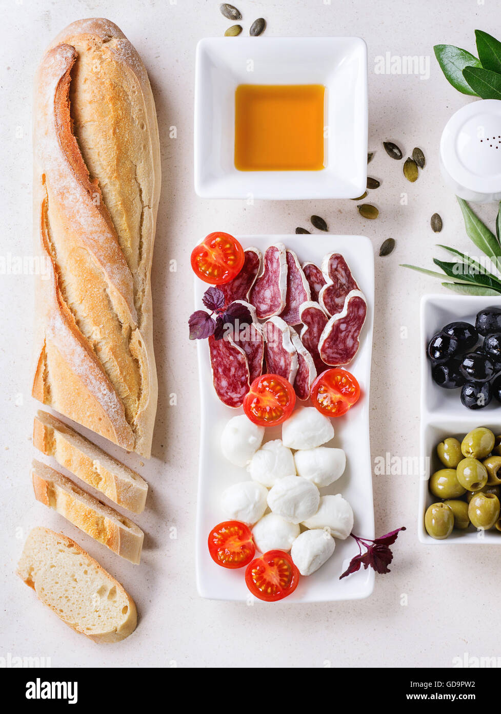 Antipasti-Snack mit Grün und Balck Oliven, Mozzarella-Käse, Wurst, Tomaten, frischen Kräutern und Brot über weißen Stein textur Stockfoto