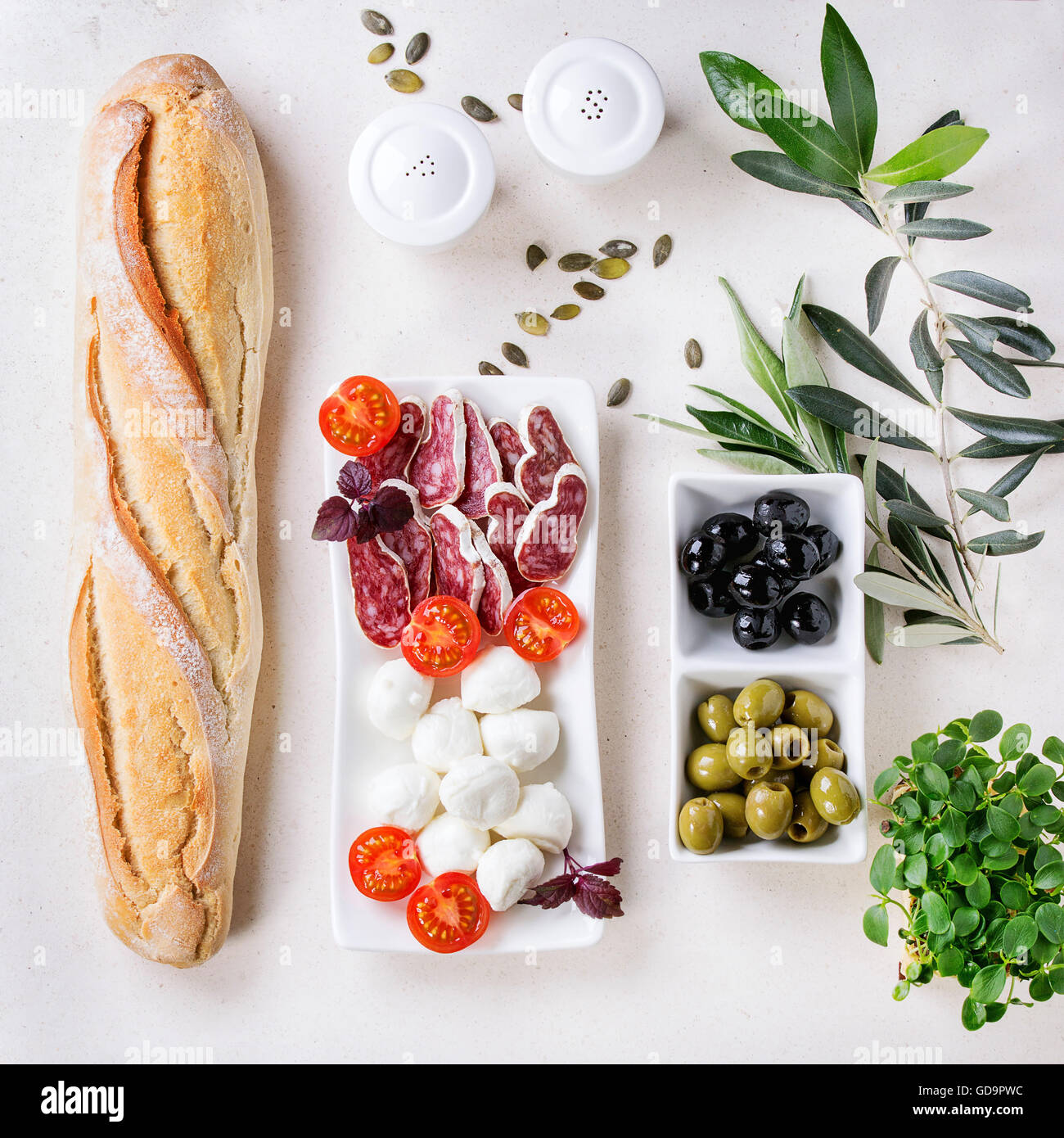 Antipasti-Snack mit Grün und Balck Oliven, Mozzarella-Käse, Wurst, Tomaten, frischen Kräutern und Brot über weißen Stein textur Stockfoto