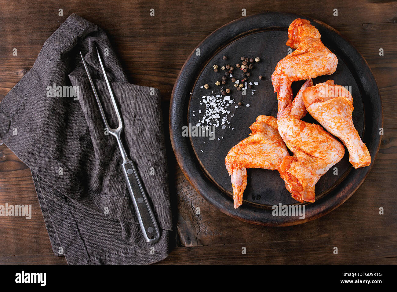 Roh mariniertes Fleisch Hähnchenflügel und Beine für Grill, serviert auf Runde Holz Schneidebrett mit Gewürzen und Vintage Fleischgabel auf t Stockfoto