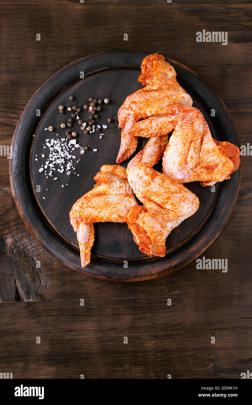 Roh mariniertes Fleisch Hähnchenflügel für Grill, serviert auf Runde Holz Schneidebrett mit Würze über dunklem Holz. Top vi Stockfoto