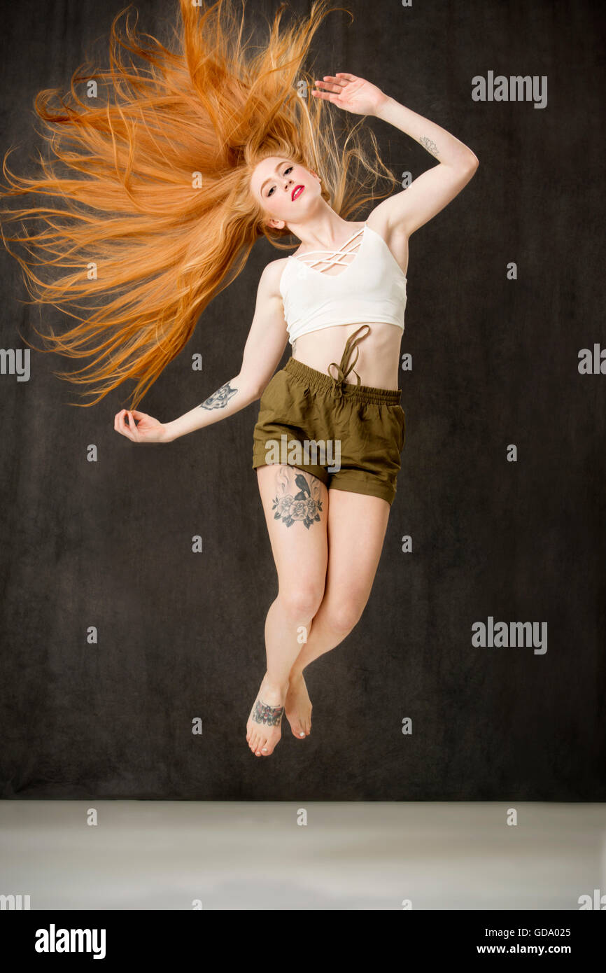 Junge Frau mit auffallend langen roten Haare und Tattoos tragen grüne Hosen und mit Haaren fanning heraus springen. Stockfoto