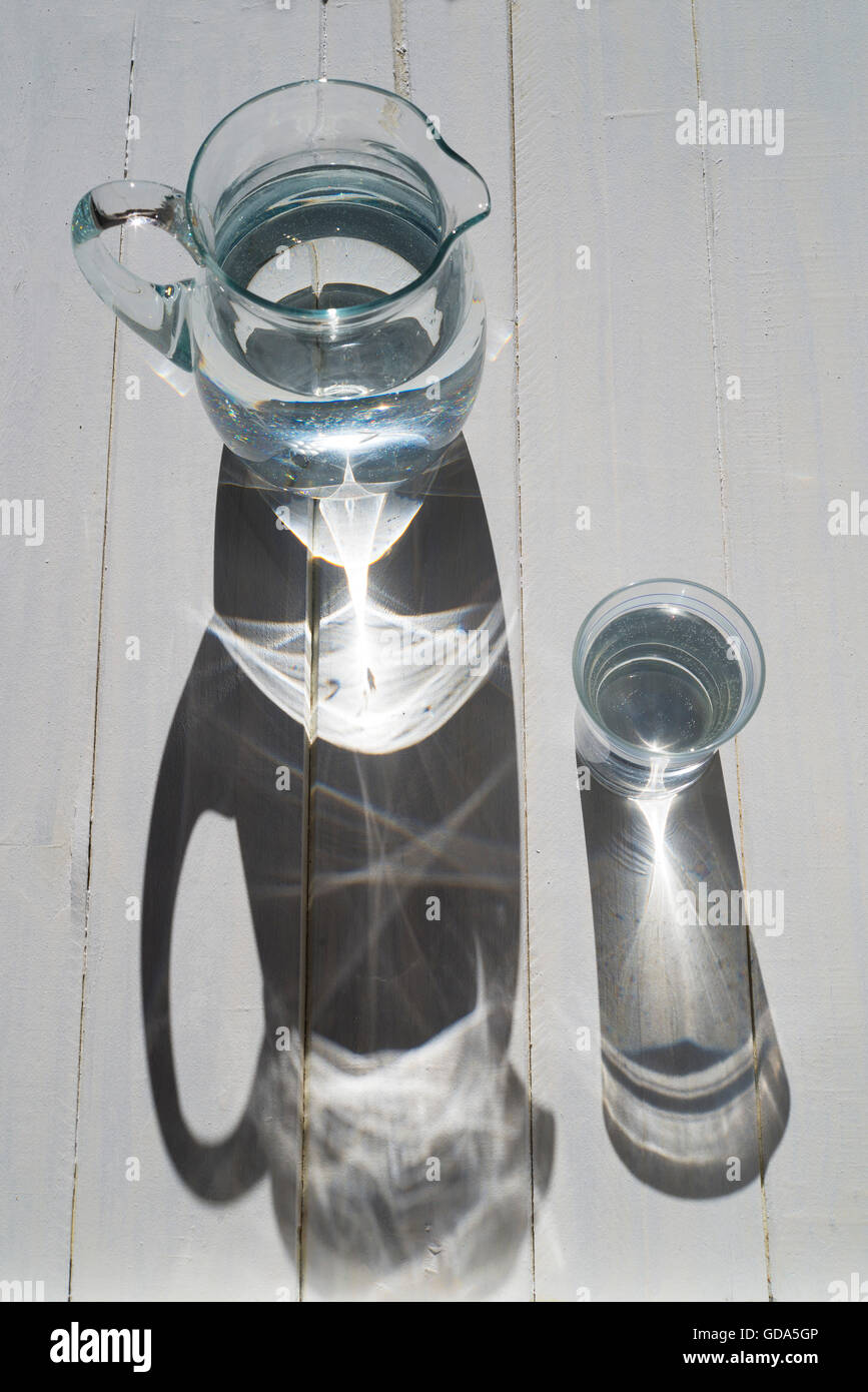 Krug und Glas Wasser auf einem Holztisch in der Sonne. Ansicht von oben Stockfoto