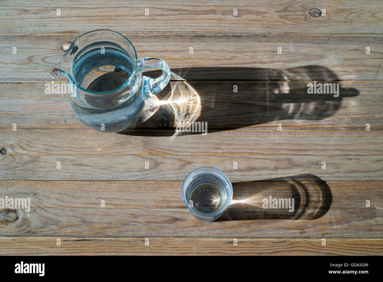 Krug und Glas Wasser auf einem Holztisch in der Sonne. Ansicht von oben Stockfoto