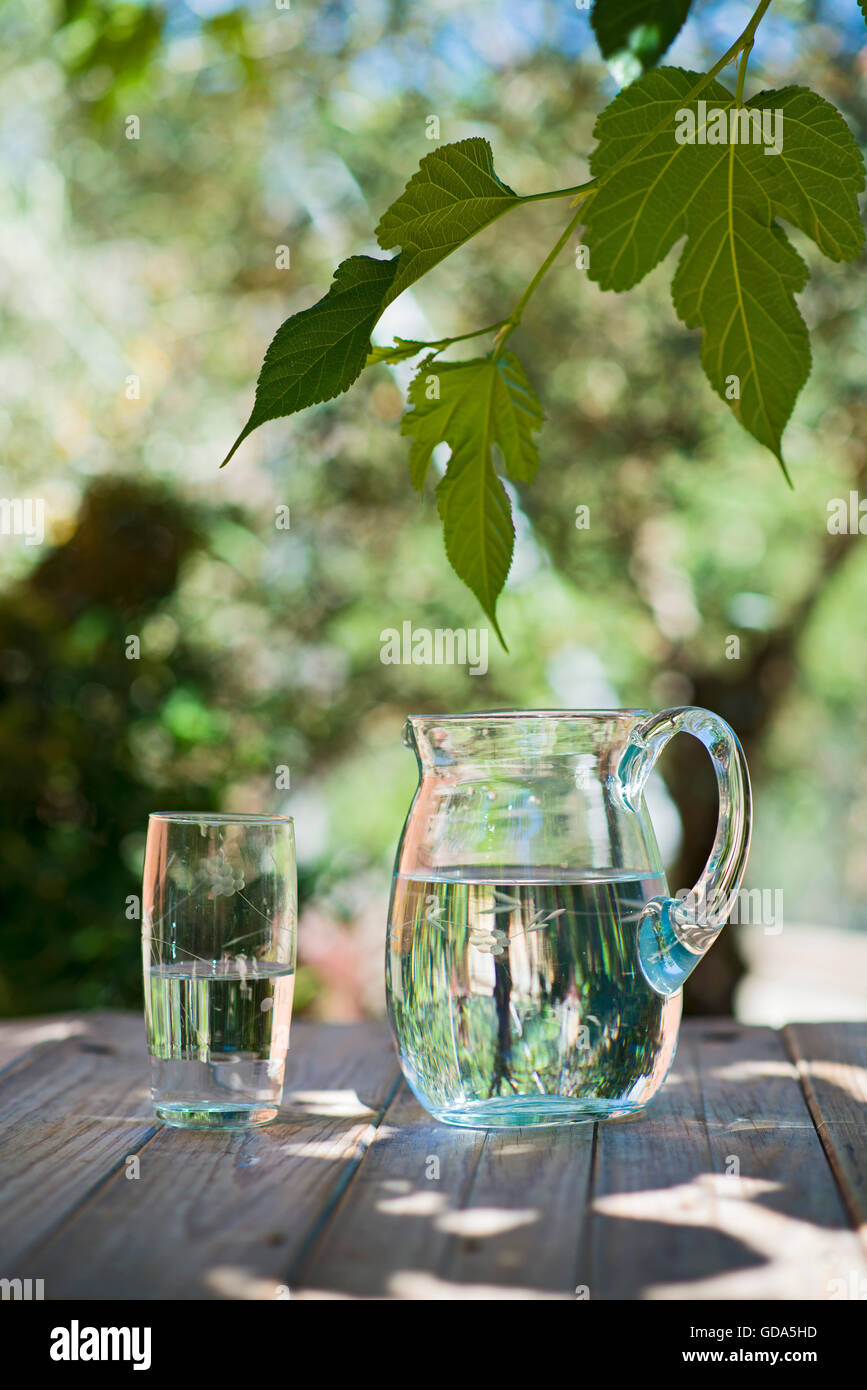 Krug und Glas Wasser auf einem Holztisch. der Garten hinter dem Haus Stockfoto