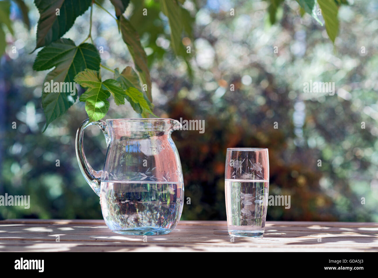 Krug und Glas Wasser auf einem Holztisch. der Garten hinter dem Haus. Textfreiraum Stockfoto