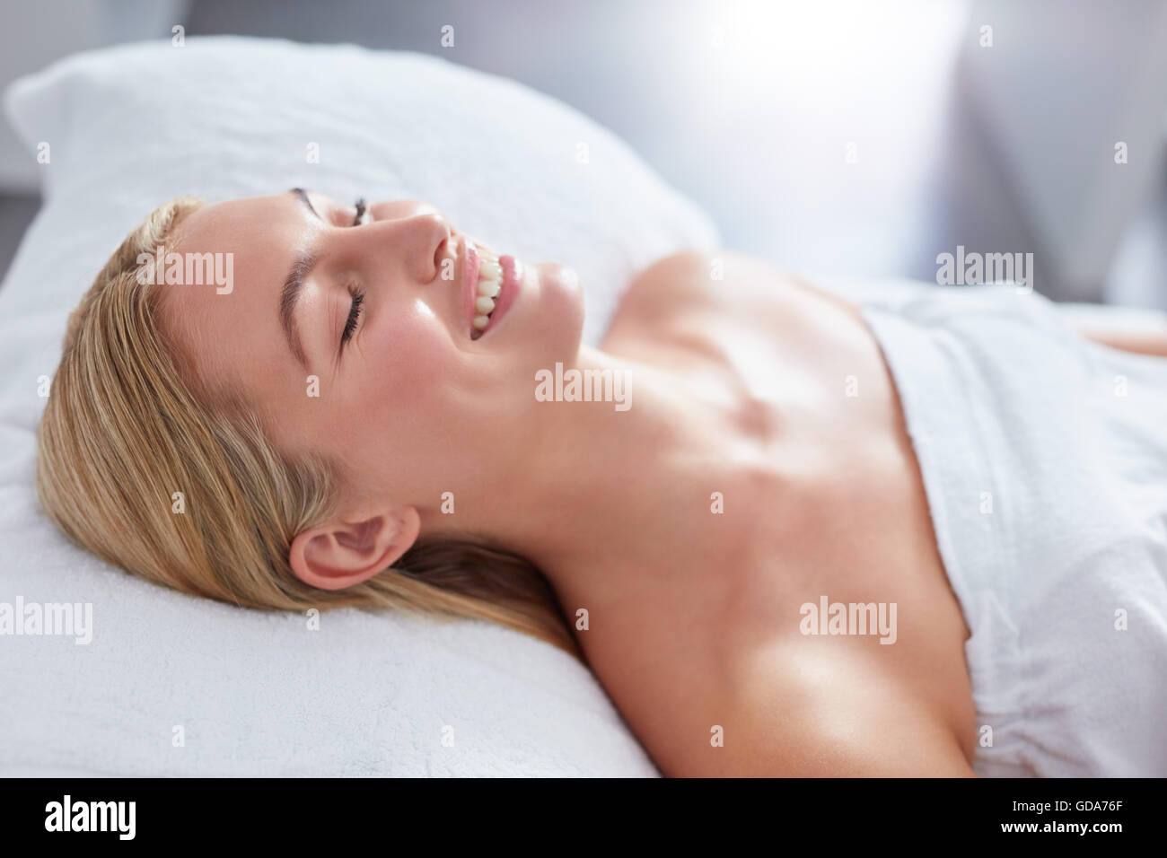 Aufnahme einer Frau in einem Day-Spa entspannen auf einem Massagetisch und lächelnd hautnah. Kaukasischen Frau in Handtuch gewickelt. Stockfoto