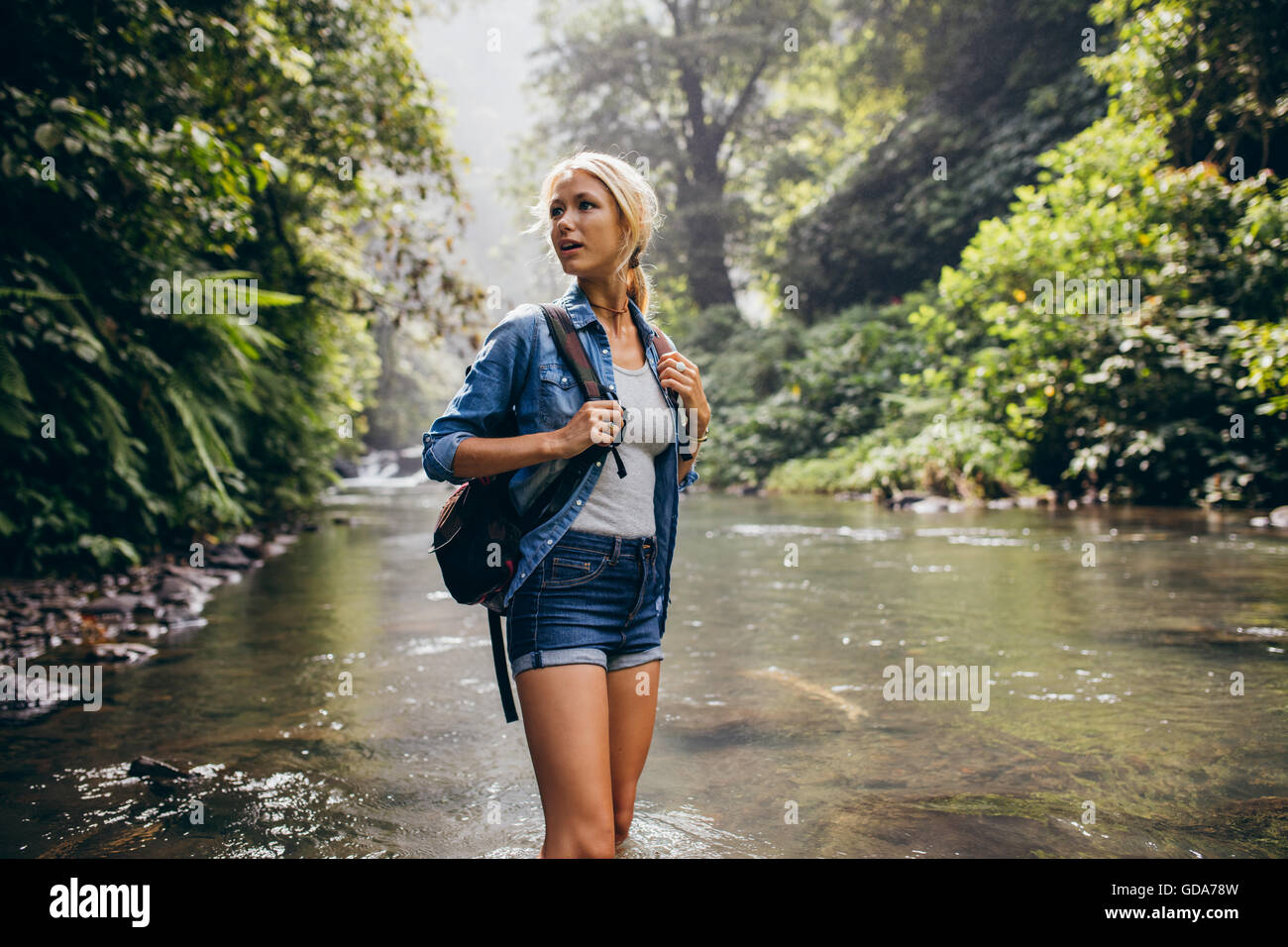 Porträt von schöne junge Frau mit Rucksack durch den Bach. Weibliche Wanderer Wandern durch den Gebirgsbach. Stockfoto