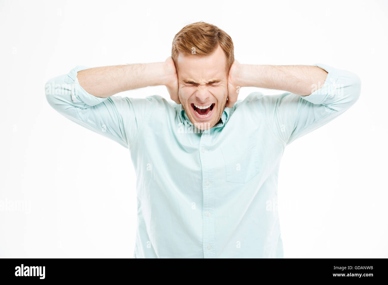 Irritierte gestresste junge Mann bedeckt Ohren von Händen und Geschrei auf weißem Hintergrund Stockfoto