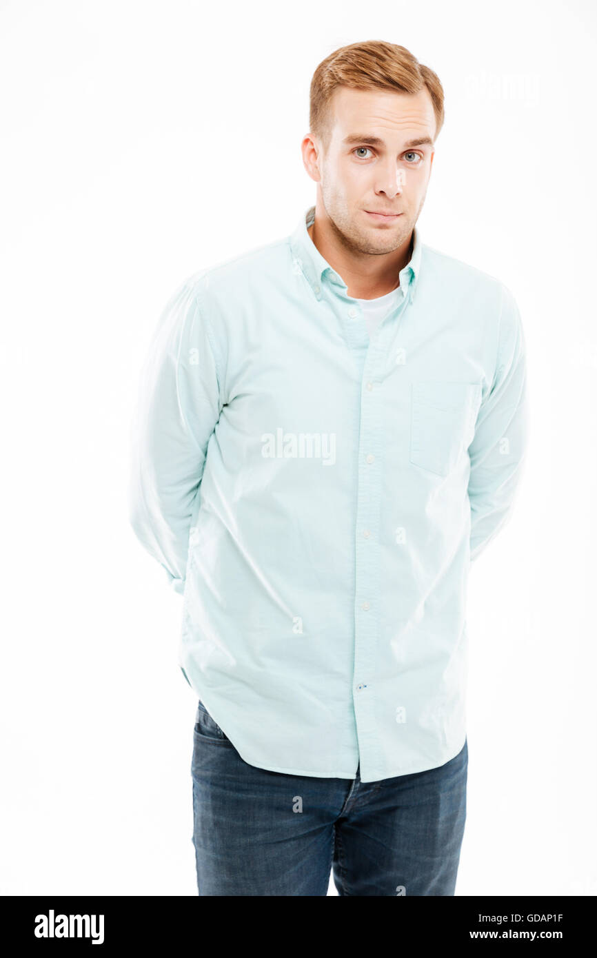 Porträt von Ernst attraktiver junger Mann mit Händen hinter dem Rücken über weißem Hintergrund stehen Stockfoto