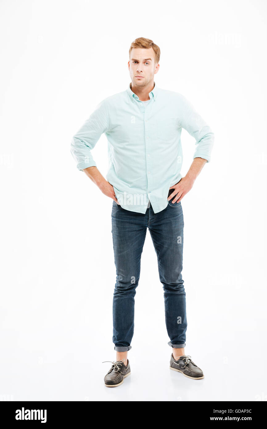 Ernsthafte verdächtige junge Mann stehend mit Händen auf den Hüften über weißem Hintergrund Stockfoto