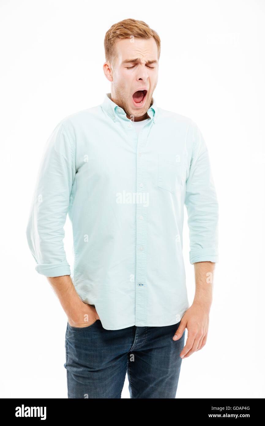 Müde, erschöpften jungen Mann stehen und Gähnen auf weißem Hintergrund Stockfoto