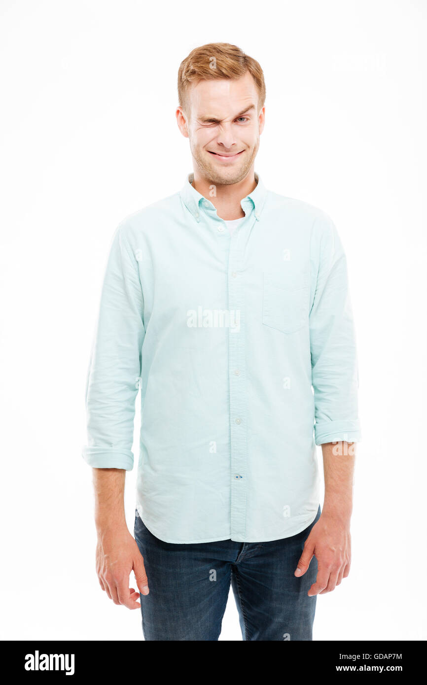 Lächelnd verspielte jungen Mann lustiges Gesicht macht und zwinkert auf weißem Hintergrund Stockfoto