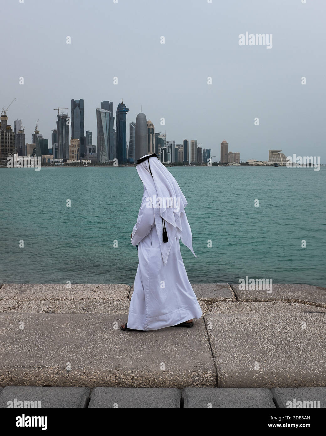 Katar Mann ein Spaziergang entlang der Corniche von Doha, mit der West Bay Skyline im Hintergrund. Stockfoto