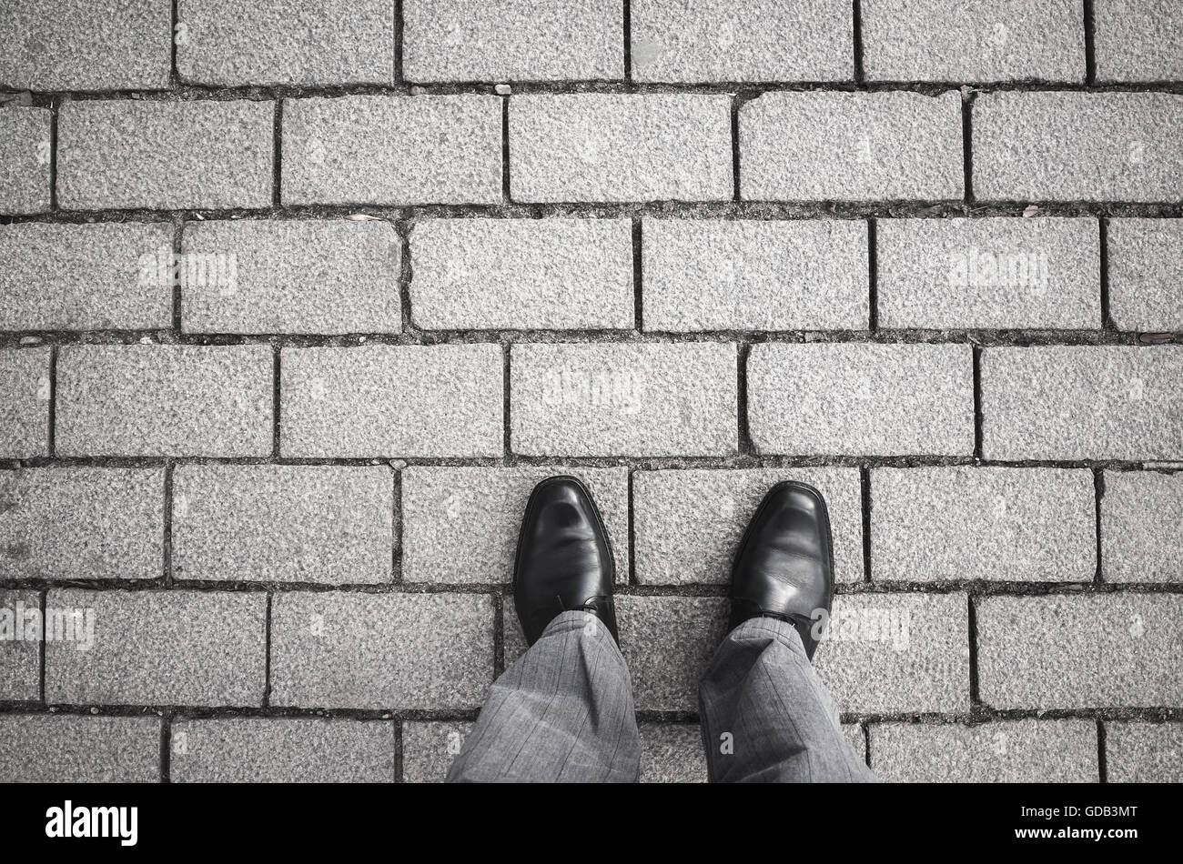 Füßen ein Städter Mannes in schwarz glänzend neu Schuhe stehen auf graue gepflasterten Straße Stockfoto