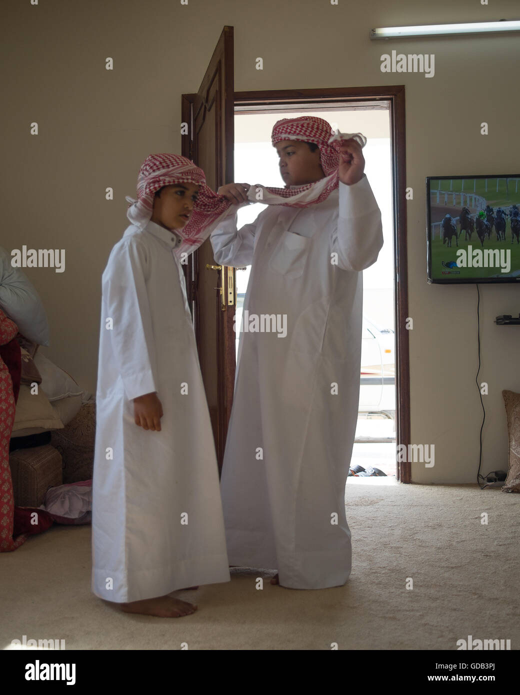 Katar junge passt seines Bruders Gutra oder traditionellen Kopf Tuch, während der Vorbereitung für ein großes Rennen bei der Camel-Rennstrecke, Al Shahiniya, nördlich von Doha, Katar. Stockfoto