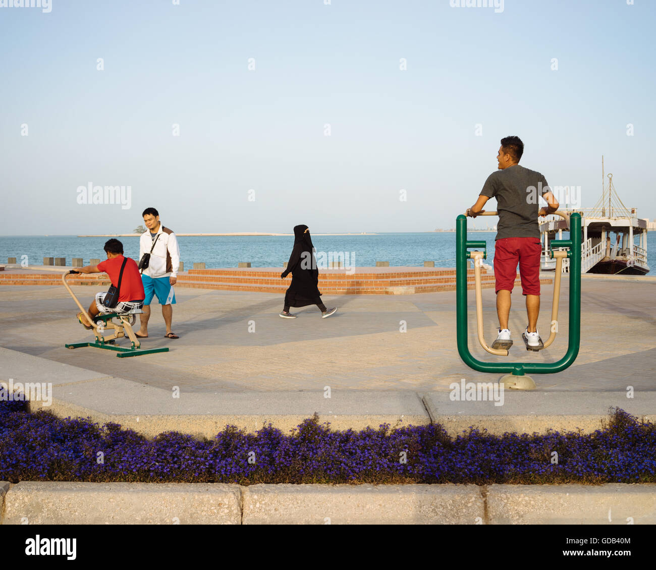 Menschen machen Verwendung von Trainingsgeräten auf Doha Corniche installiert, lokale Frau in Laufschuhen Spaziergänge Streicheleinheiten. Stockfoto
