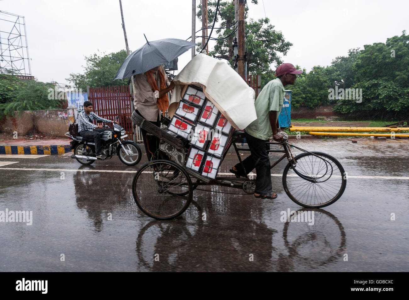 Zyklus-Rikscha-Fahrer mit einem Mann und voller Last-Boxen in Agra, Uttar Pradesh, Indien Stockfoto