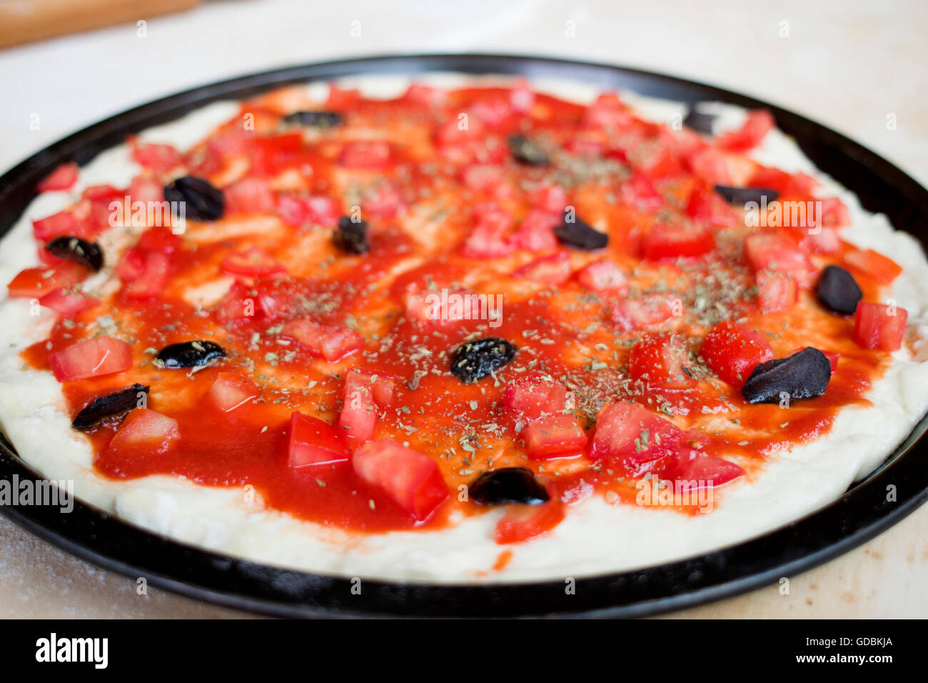 Rohe Pizza mit Tomaten und schwarzen Oliven Stockfoto