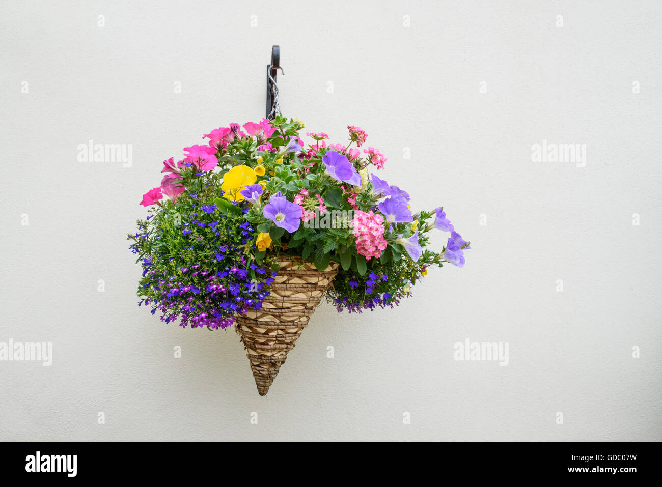 Bunte hängende konische geformte Blume Weidenkorb auf einem Creme farbigen Wand Stockfoto