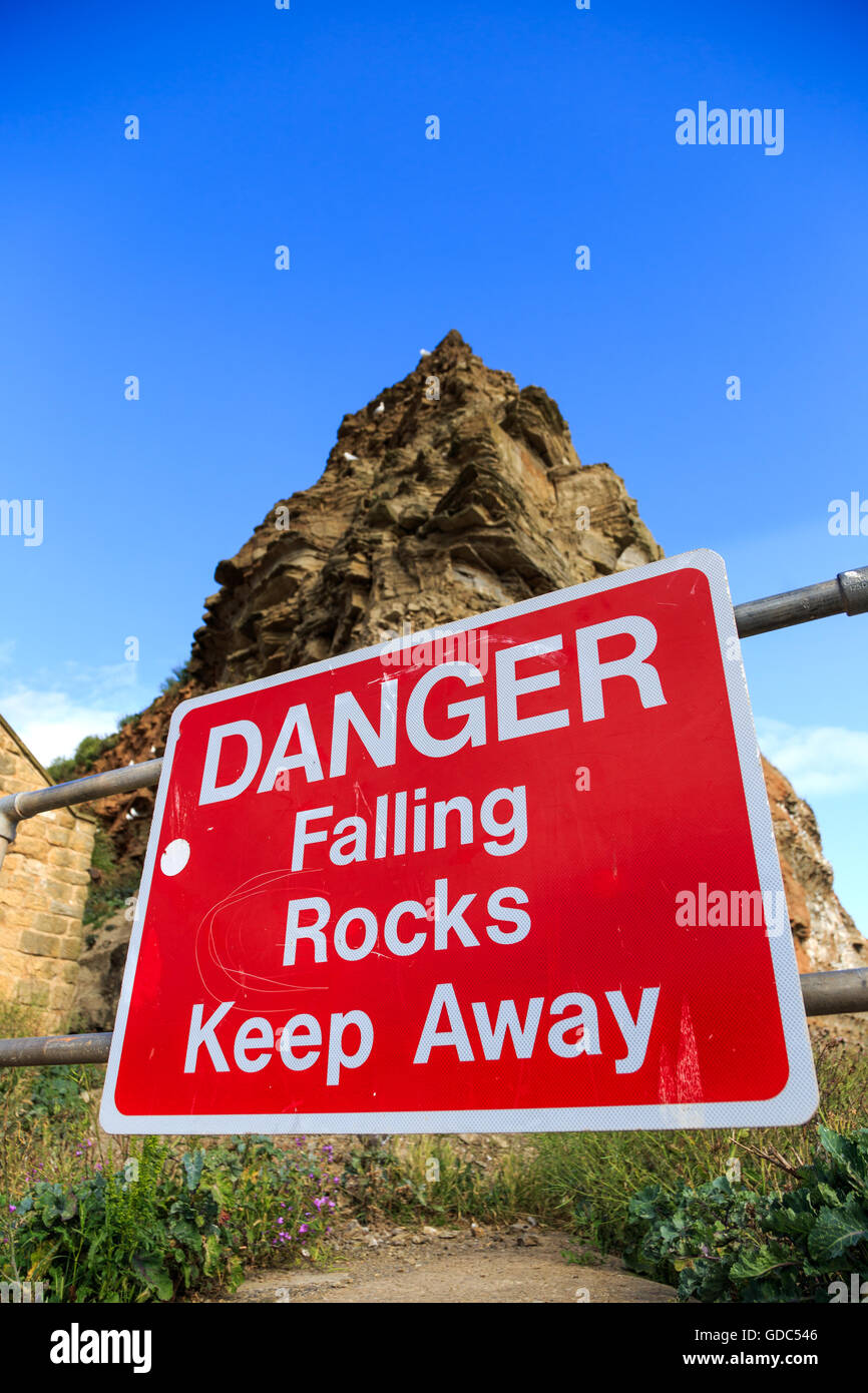 Ein "Steinschlag Gefahr fernzuhalten" Schild mit Klippen hinter. In Staithes, North Yorkshire, England. Stockfoto