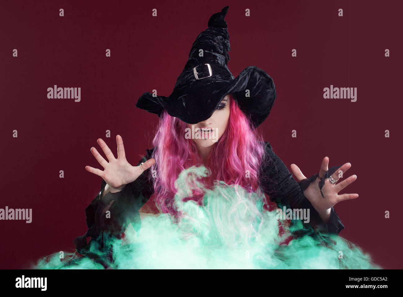 Gruselige Hexe mit roten Haaren führt Magie über den grünen Rauch. Halloween, Horror-Thema. Stockfoto