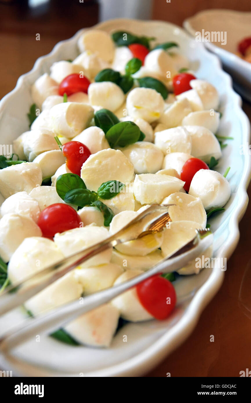 Teller mit italienischen Caprese-Salat mit Mozzarella, Basilikum und Tomaten auf einem Buffet-Tisch mit einer Zange zum servieren Stockfoto