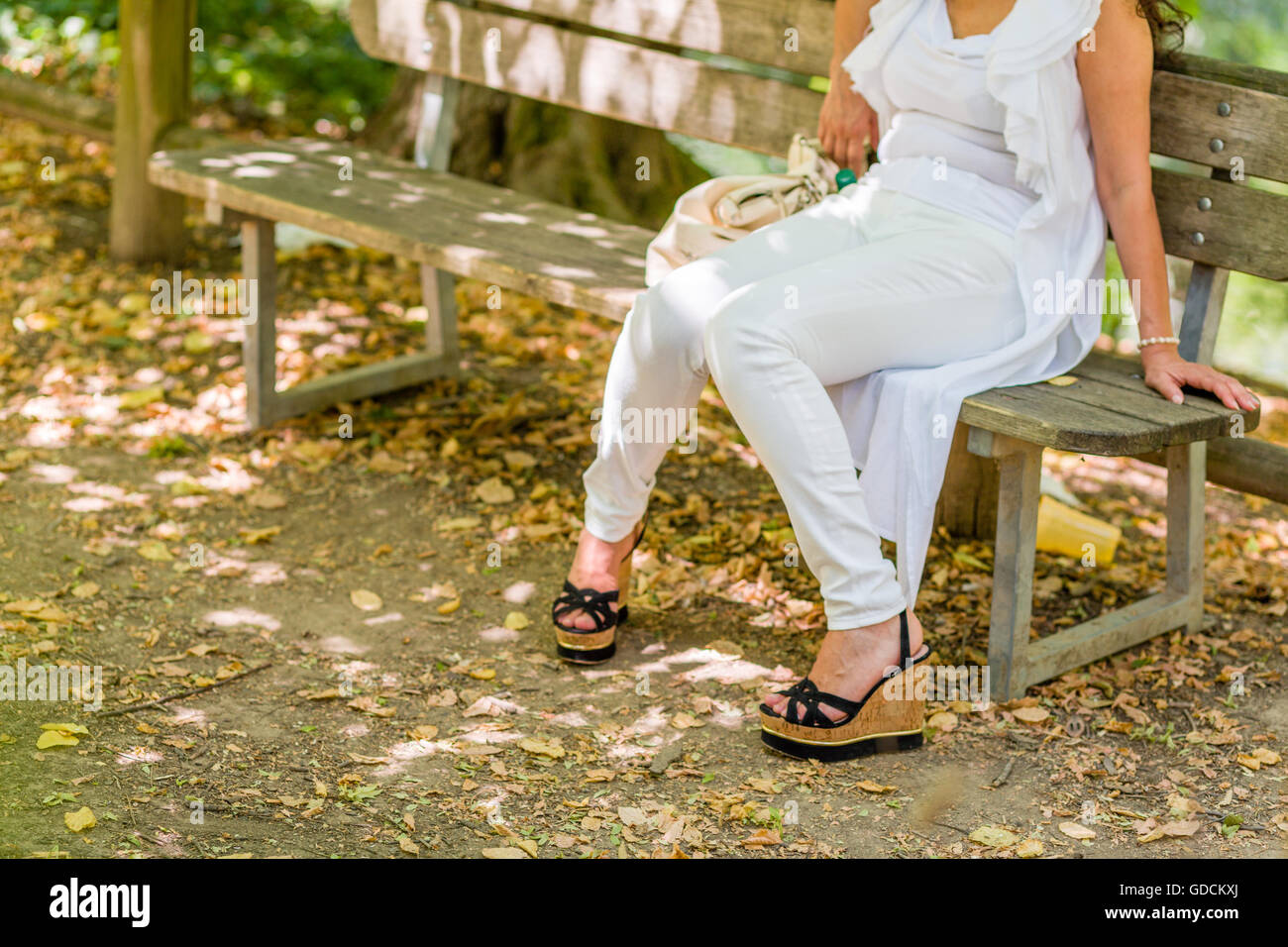 Beine der Frau sitzen auf Bank in weißer Hose und hohe Plateau-Schuhe, Knie berühren einander Stockfoto