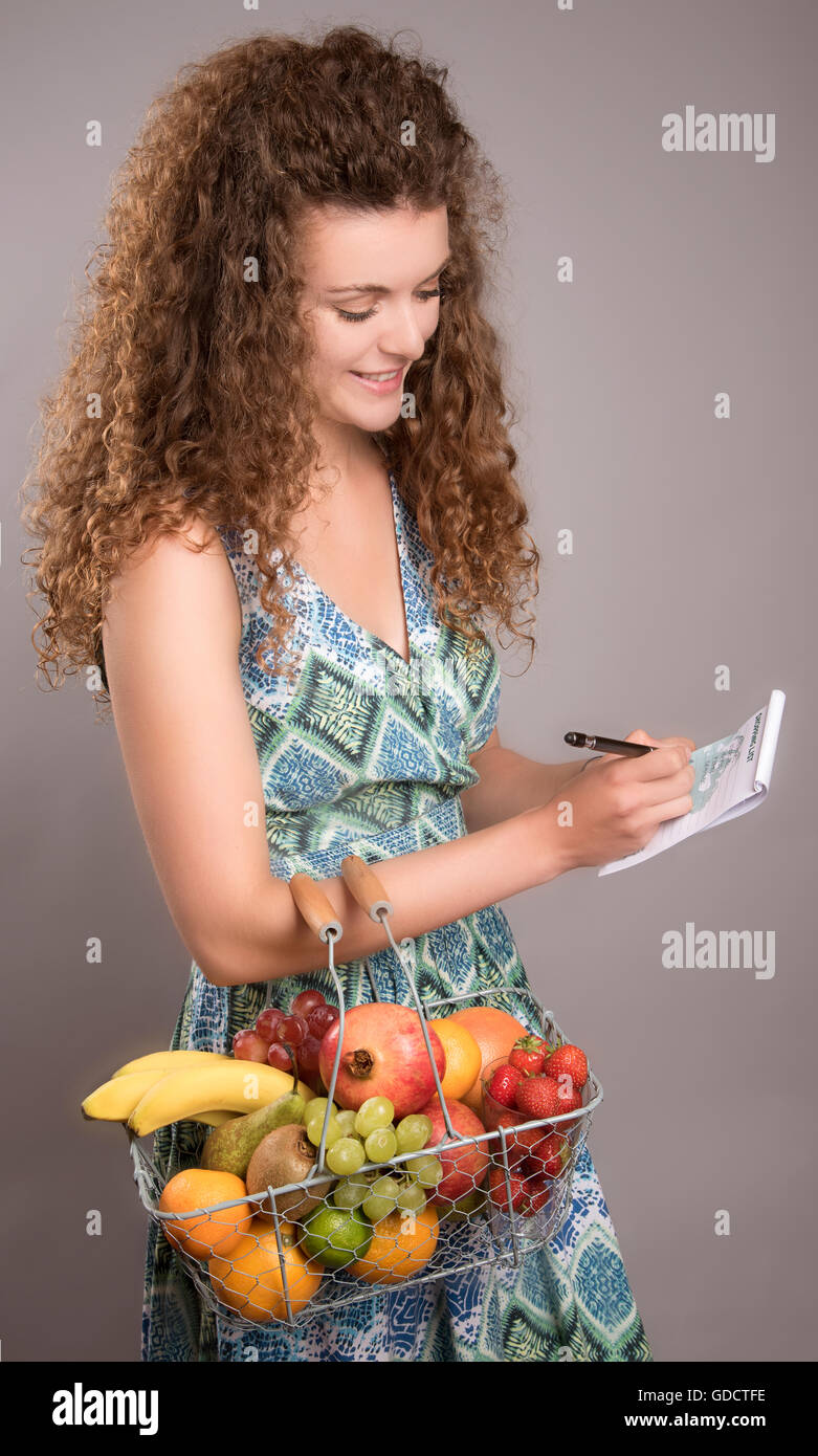 Junge Frau mit einem Warenkorb von frischen Früchten Überprüfung eine Einkaufsliste Stockfoto