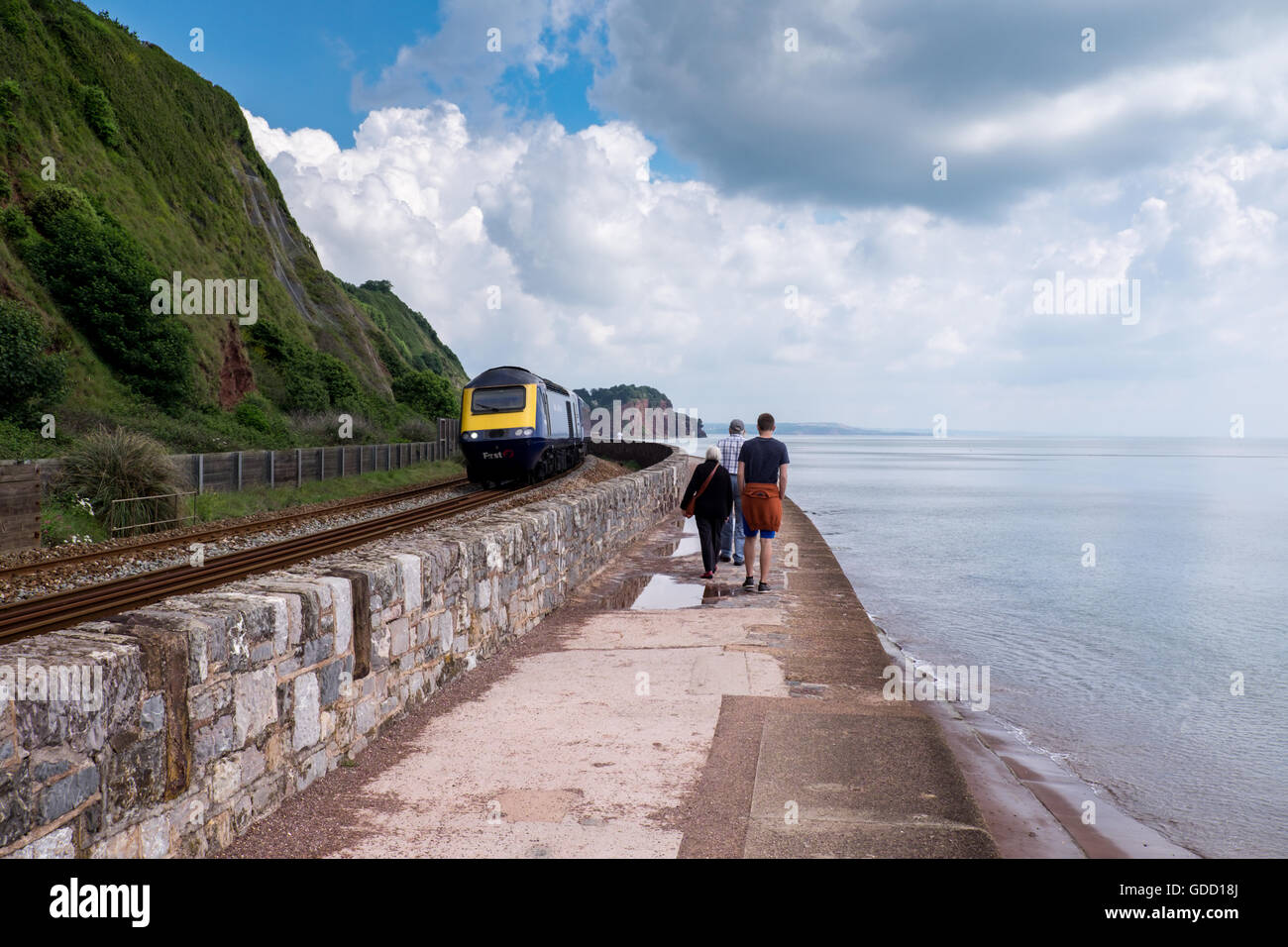 Menschen zu Fuß entlang dem Deich mit einem herannahenden 125 Zug in Teignmouth in der Nähe von Dawlish, Devon, England. Stockfoto