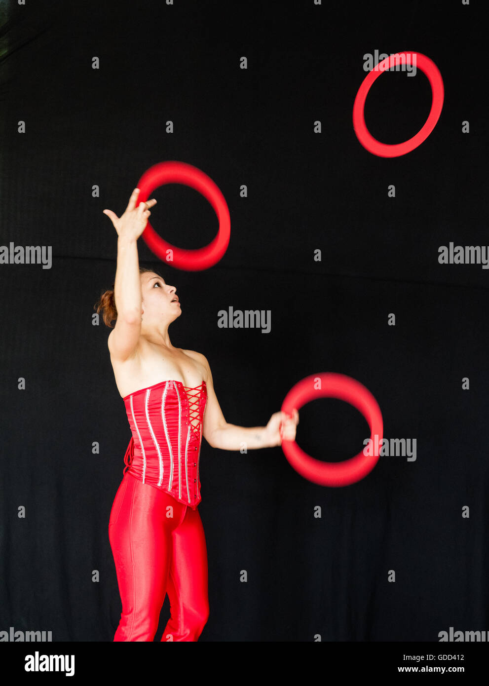 Junge weibliche Jongleur in roten Baske werfen und fangen rote Jonglier-Ringe Stockfoto