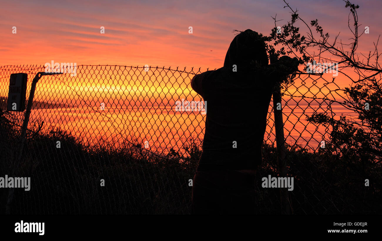 Silhouette der Person stützte sich auf Metallzaun bei Sonnenaufgang Blick auf Meer, Malibu, California, Amerika, USA Stockfoto