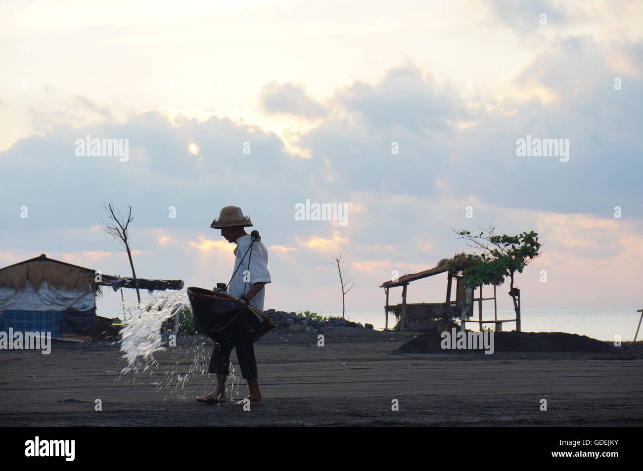Salz Bauer spritzt sich Wasser auf den Sand, Bali, Indonesien Stockfoto